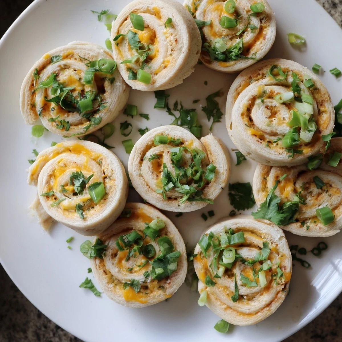 Spicy jalapeno popper pinwheels arranged on a serving platter, garnished with fresh green onions