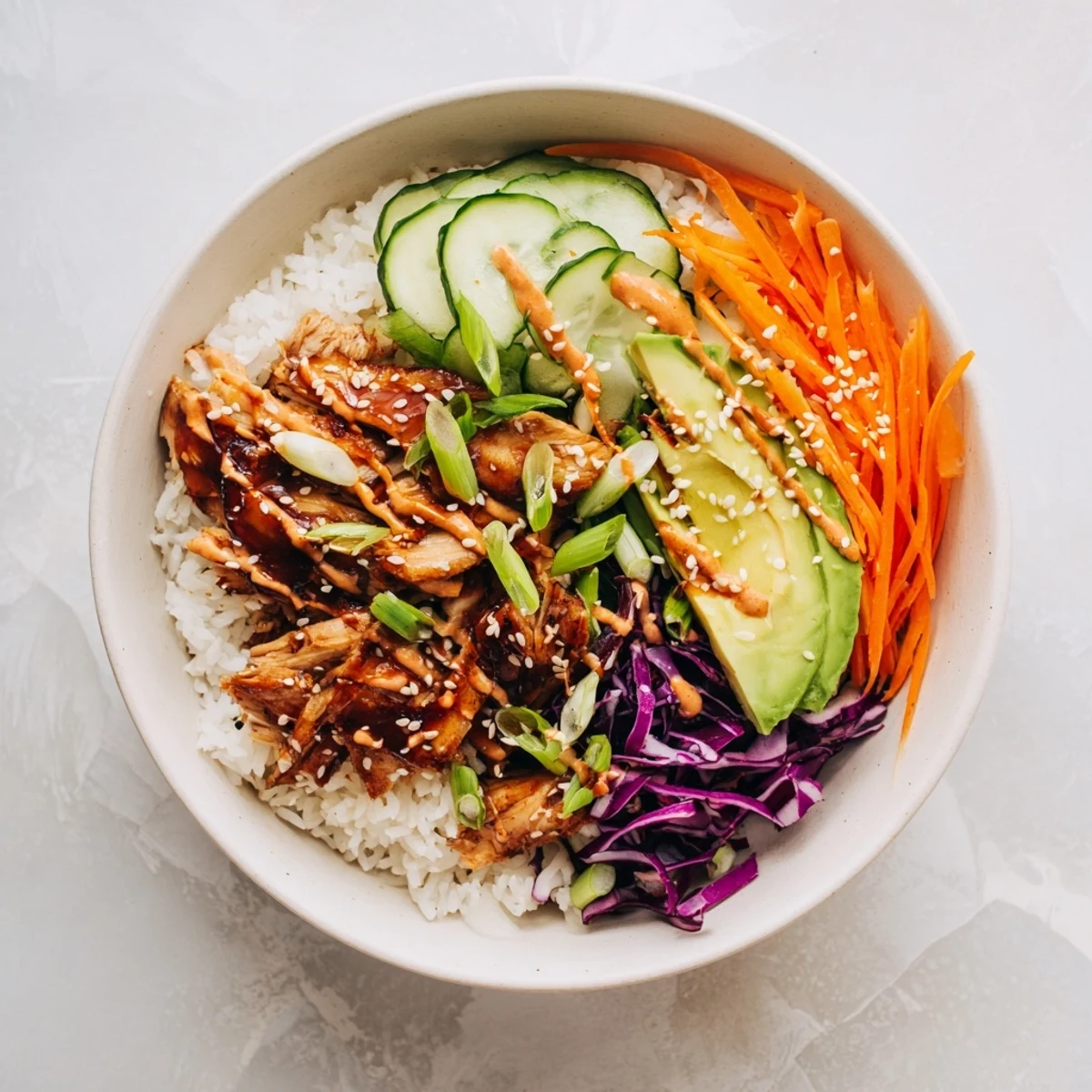 Vibrant Korean BBQ Chicken Bowl arranged with sliced avocado, purple cabbage, carrots, cucumber, and sesame seed garnish