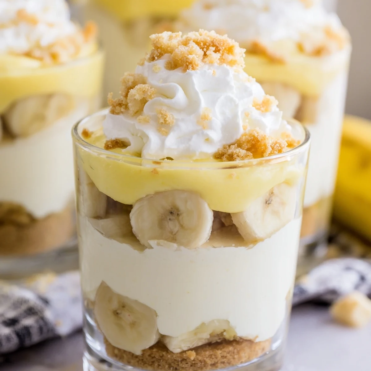 Individual no bake banana pudding cheesecake cups topped with whipped cream and crunchy crumbs