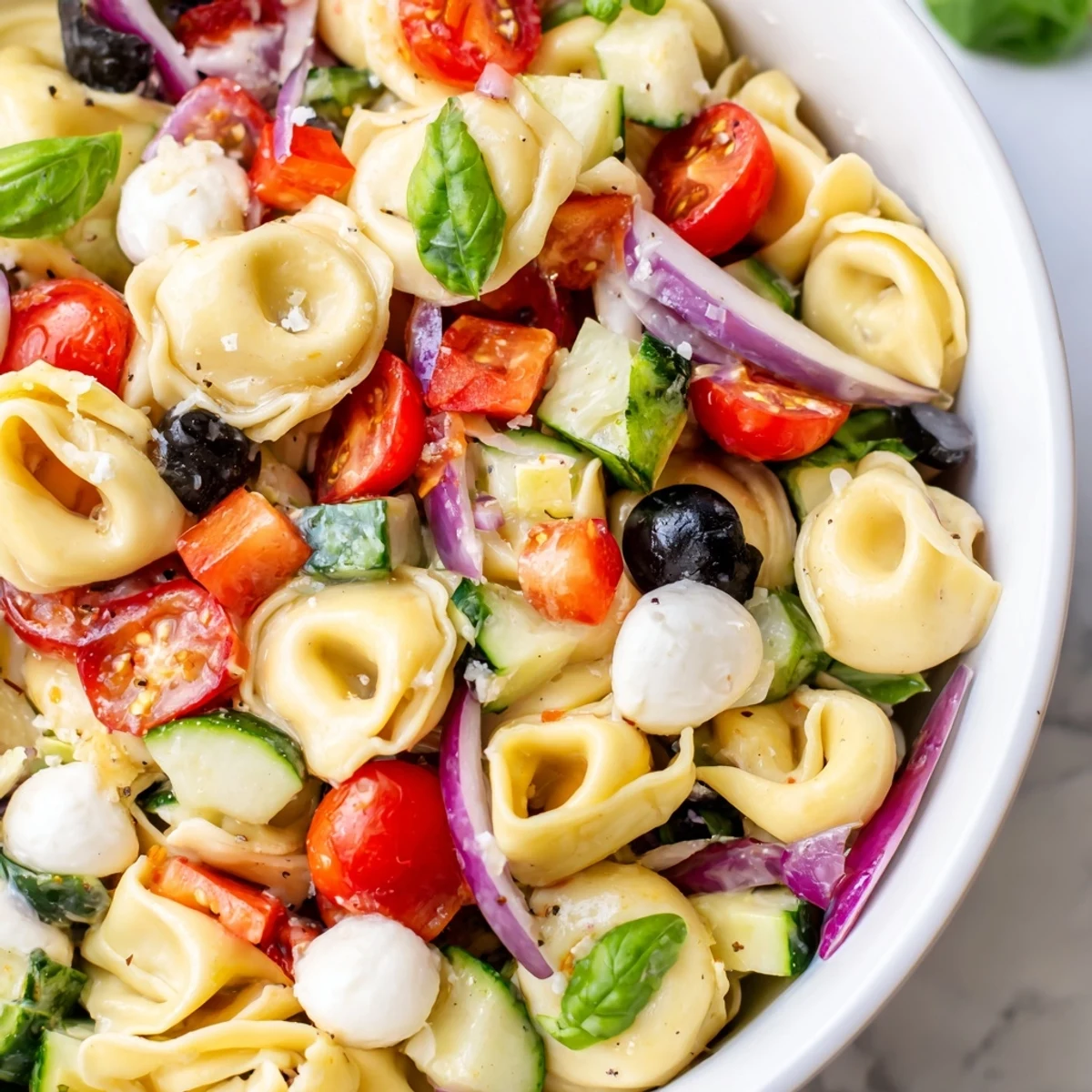 Creamy cheese tortellini salad tossed with crisp vegetables and fresh basil on a white platter