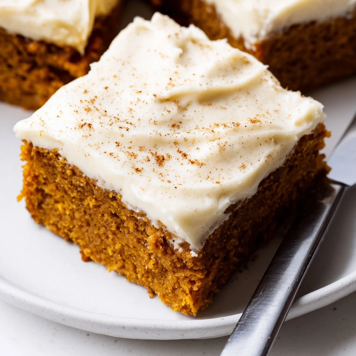 Thick slice of pumpkin bars with cream cheese frosting on a rustic cutting board