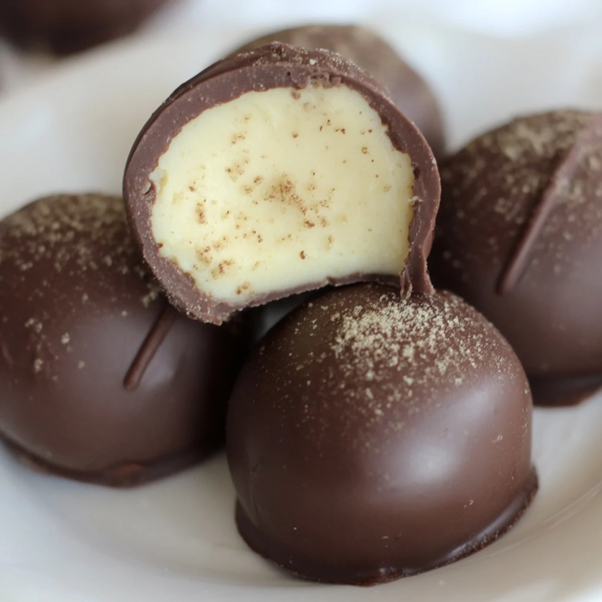 Stacked Dark Chocolate Eggnog Truffles on parchment, soft creamy centers revealed