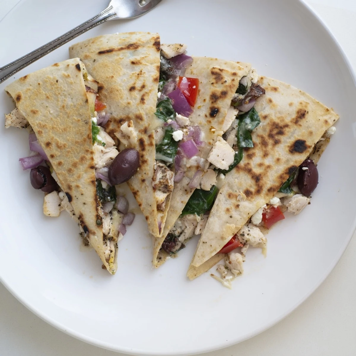 Golden brown Greek chicken quesadilla stuffed with melty mozzarella feta cheese and Mediterranean vegetables