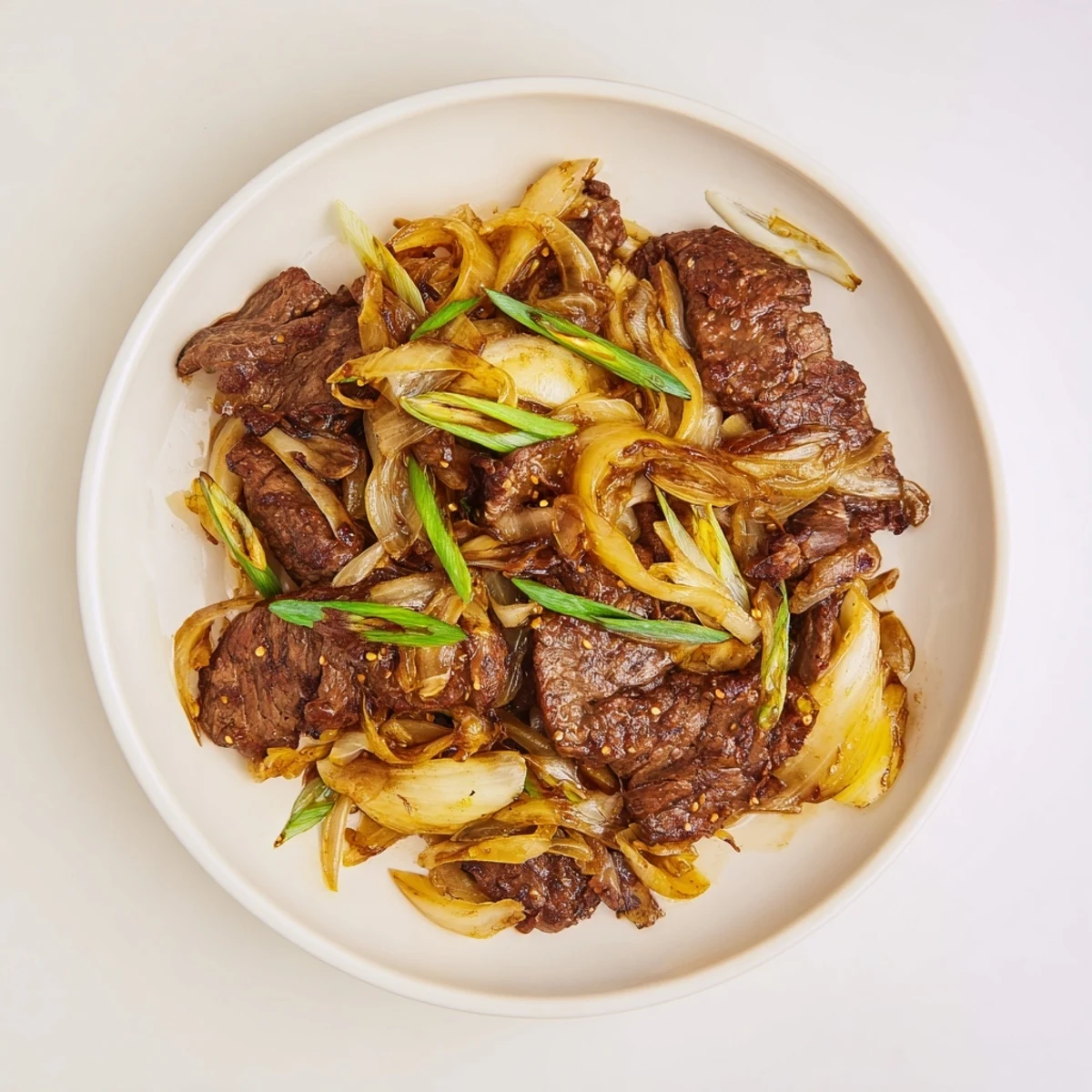 Golden crispy beef and caramelized onions stir fry plated over white rice with fresh green onion garnish