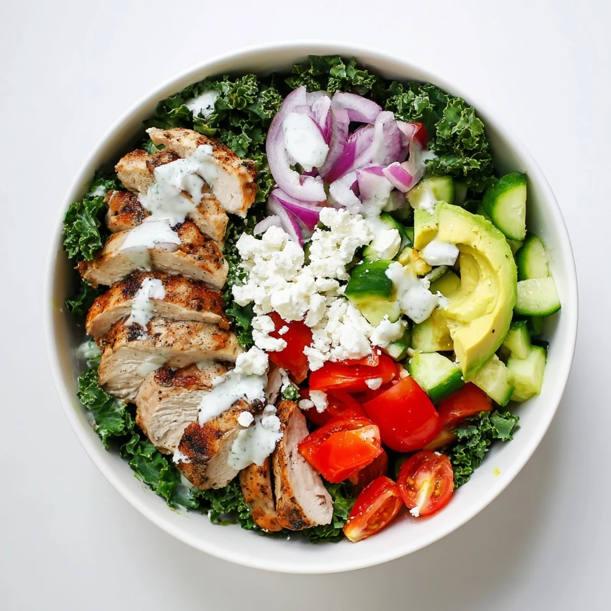 Healthy marinated kale and chicken bowls arranged with cucumber, red onion, and feta