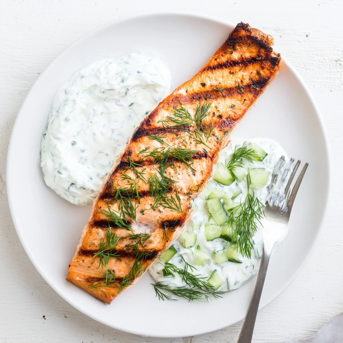 Golden grilled salmon fillets with char marks topped with creamy cucumber dill yogurt sauce
