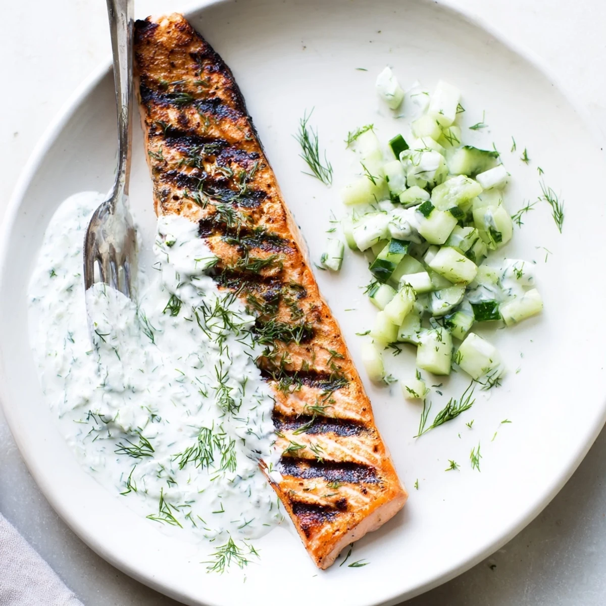 Perfectly grilled salmon fillets served with refreshing cucumber dill sauce on white plate