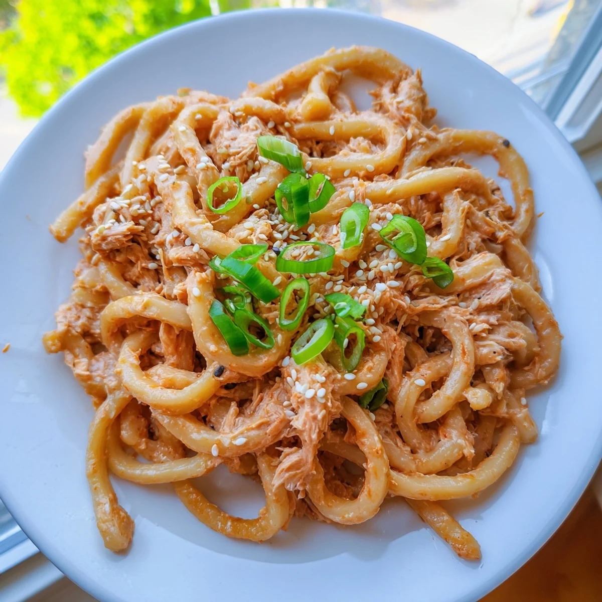 Chewy udon noodles coated in creamy spicy tuna sauce with green onion garnish