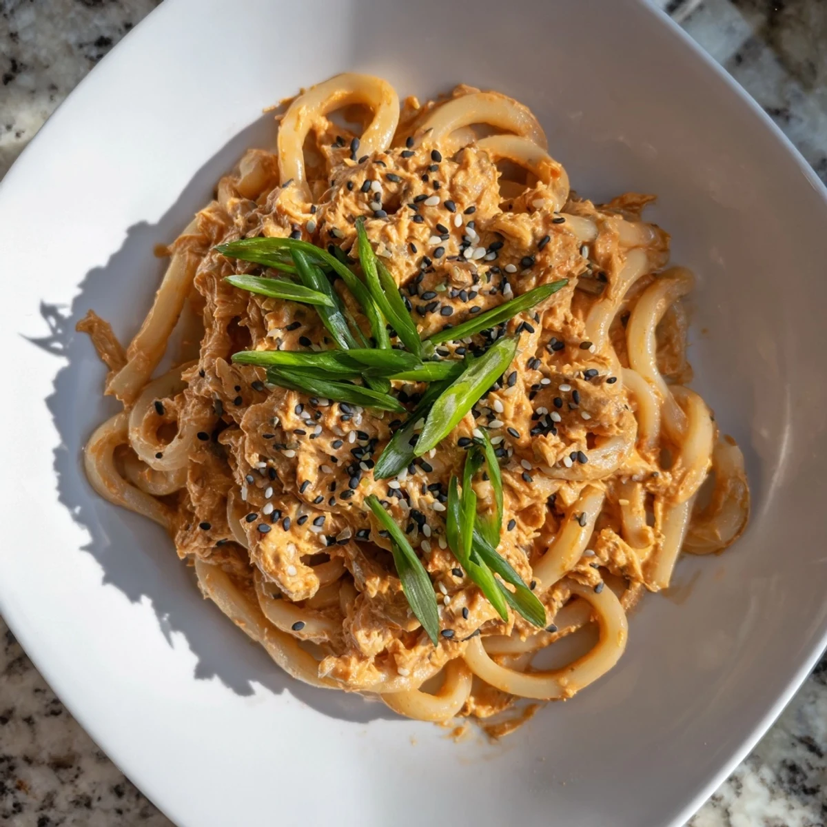 Japanese fusion spicy tuna udon featuring thick noodles and vibrant scallion toppings