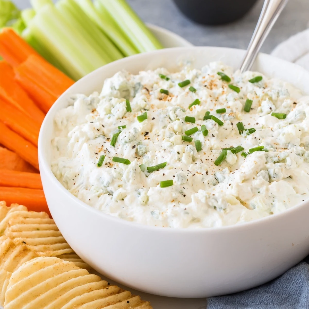 Creamy blue cheese dip in a rustic bowl with fresh celery sticks and chips nearby