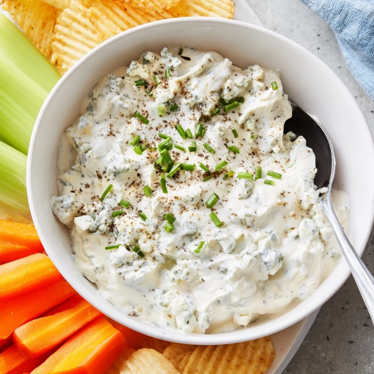 Thick blue cheese dip topped with crumbled cheese and chopped chives in a ceramic dish