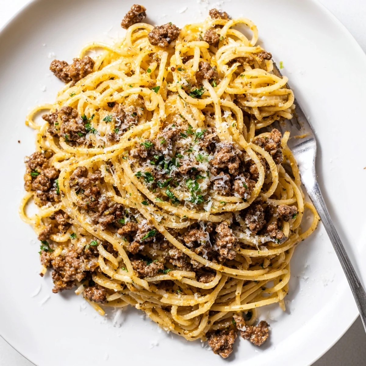 Garlic Butter Pasta With Ground Beef topped with Parmesan cheese and fresh parsley on a white plate