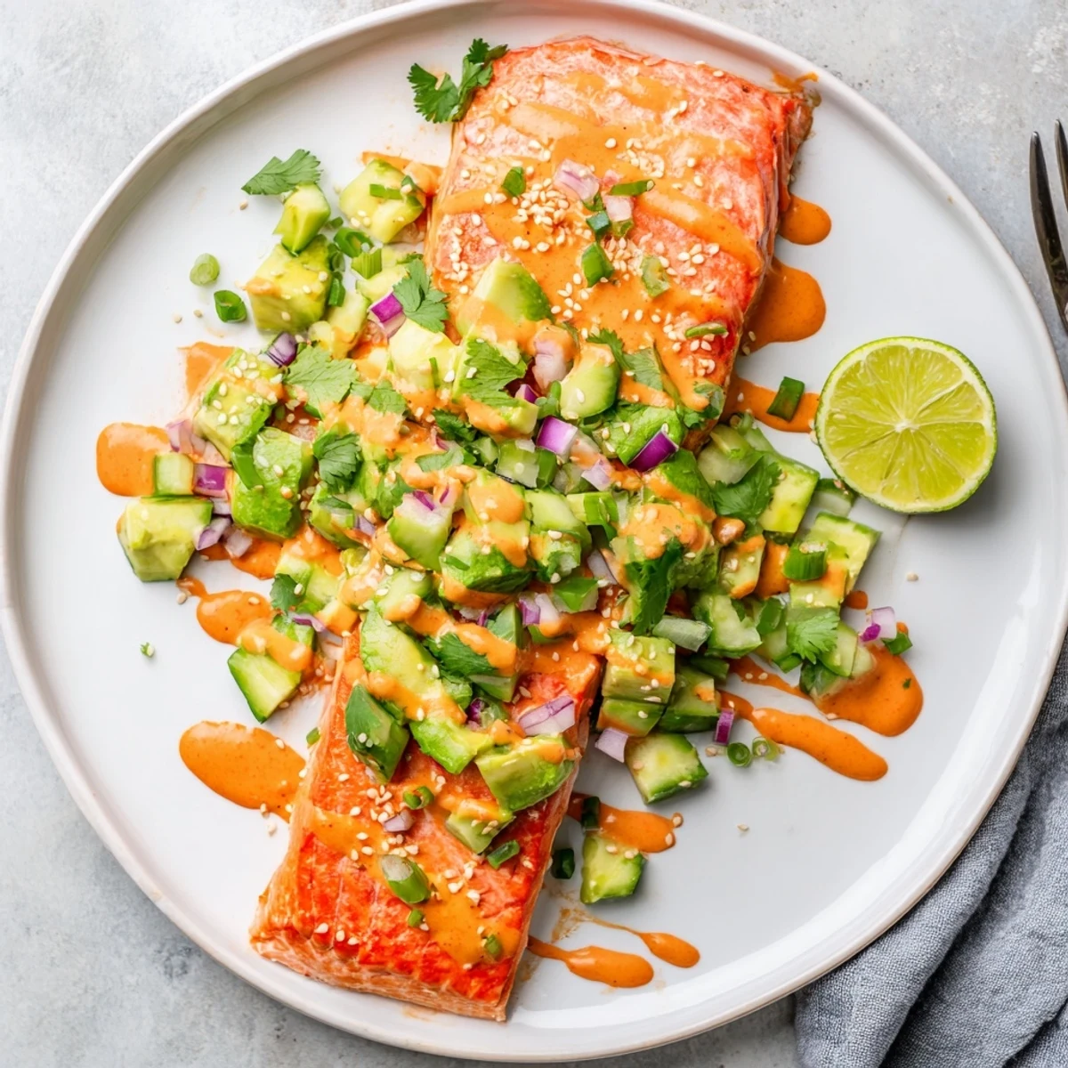 Spicy Bang Bang Salmon drizzled with creamy sauce beside bright avocado cucumber salsa