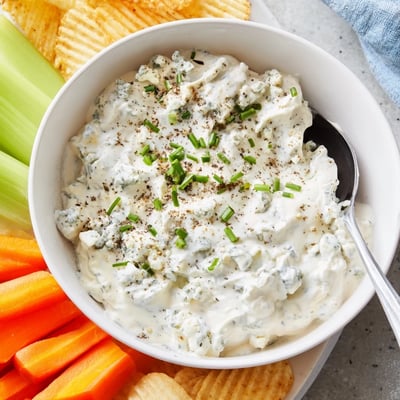 Thick blue cheese dip topped with crumbled cheese and chopped chives in a ceramic dish