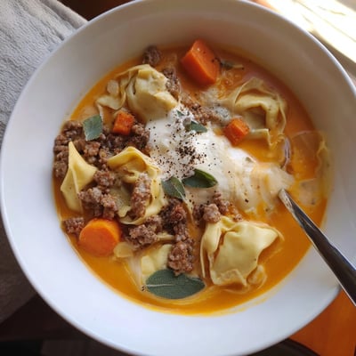 Steaming bowl of butternut squash sausage tortellini soup with melted cheese swirl and fresh sage garnish